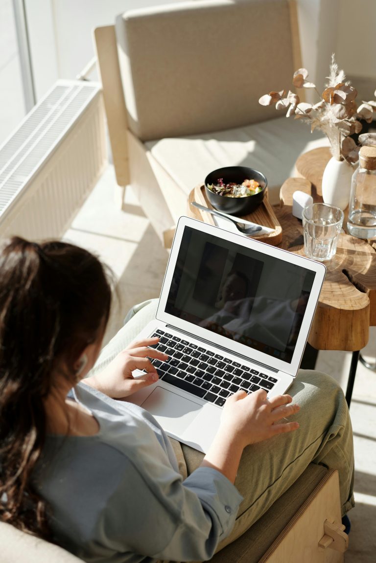 Woman enjoying remote work on a laptop in a cozy home setting with natural light.